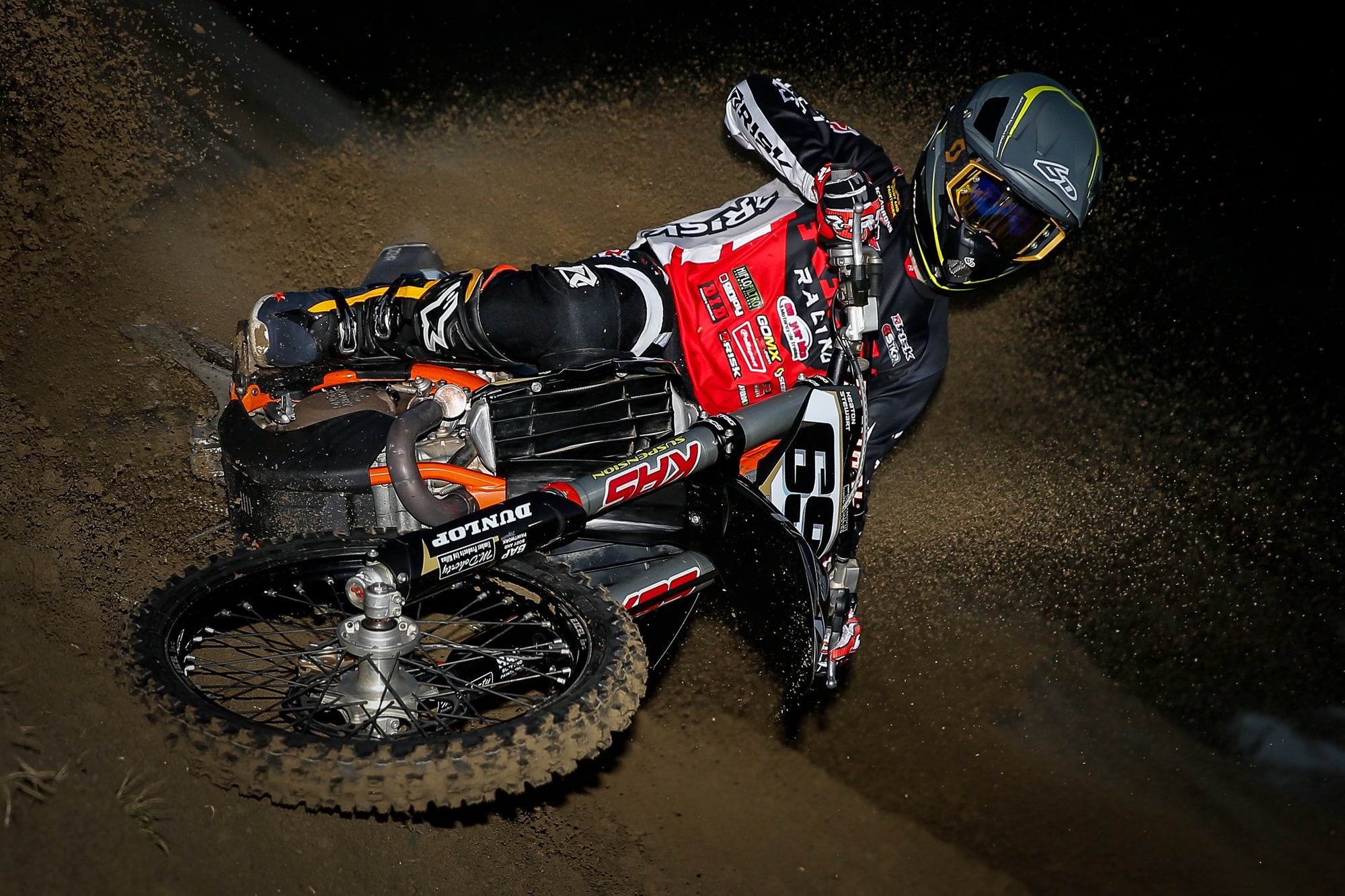 Motocross rider hitting a turn in the sand in risk racing ventilate v2 series gear. Sand flying from the rear tire of the motorcycle.