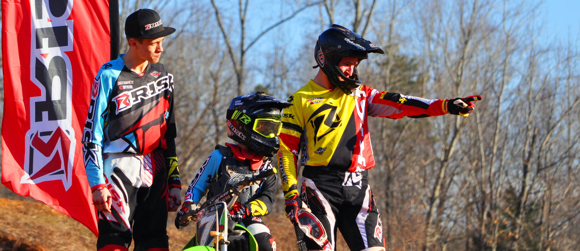 Risk Racing team standing on the landing of a track feature in their signature Ventilate V2 Mix-n-match motocross protective gear. One team member is pointing out another track feature to his teammates.