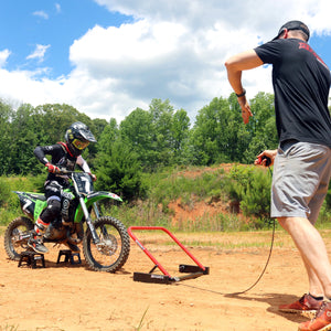 child on a dirt bike in full motocross gear lined up at a Holeshot Starting Gate Manual version. Dad is holding the trigger and signaling his son to get ready for the gate drop.